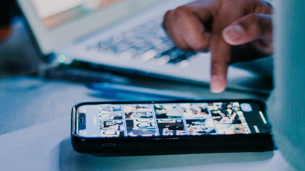 Fingers reaching towards a mobile phone, laptop in the background
