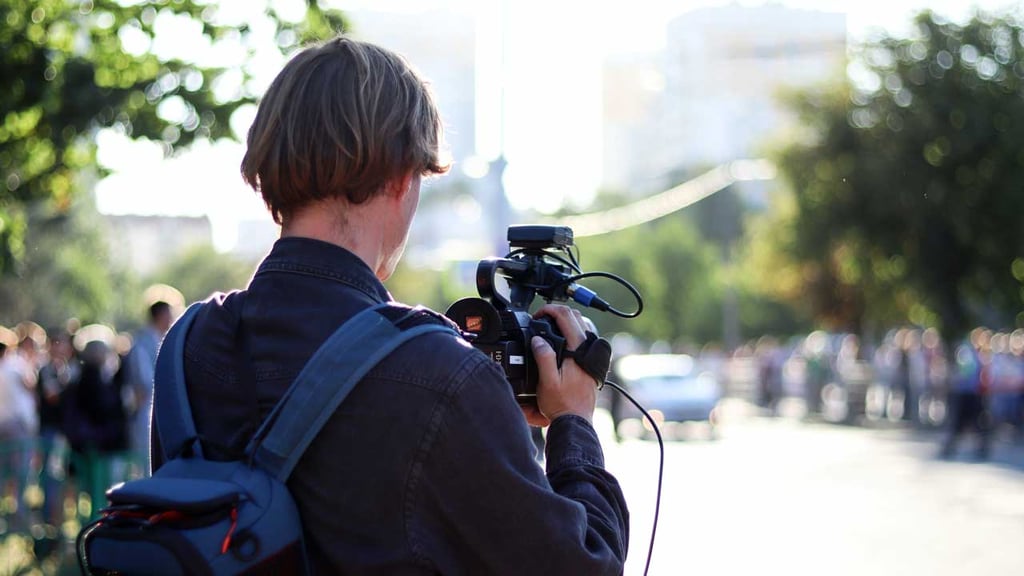 Back of a man in foreground with a video camera filming the street in front of him
