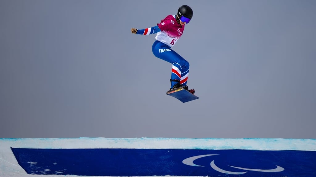 French Para snowboard athlete Cecile Hernandez performing a jump during a Paralympic snowboard event at the Beijing 2022 Winter Paralympic Games.